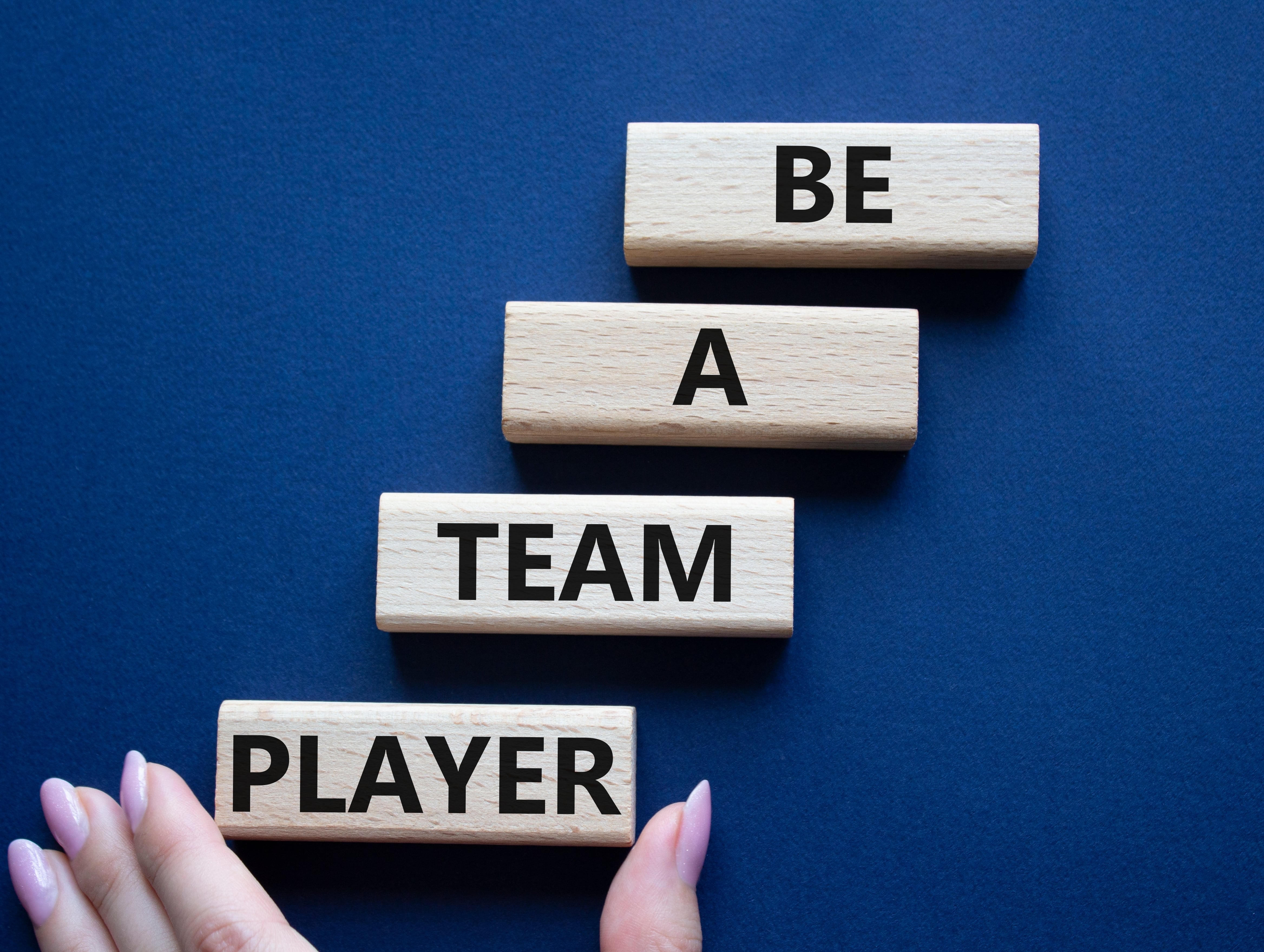 Be a team player symbol. Concept words Be a team player on wooden blocks. Businessman hand. Beautiful deep blue background. Be a team player concept. 