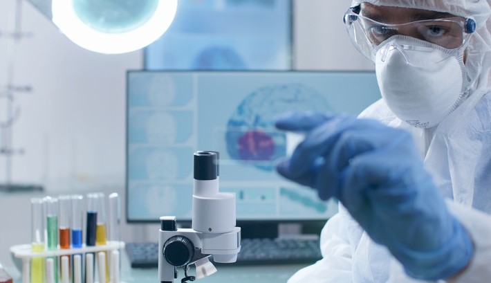 Clincial researcher holding microscope slide analyzing blood sample working at coronavirus vaccine development during virus examination in microbiology hospital laboratory.