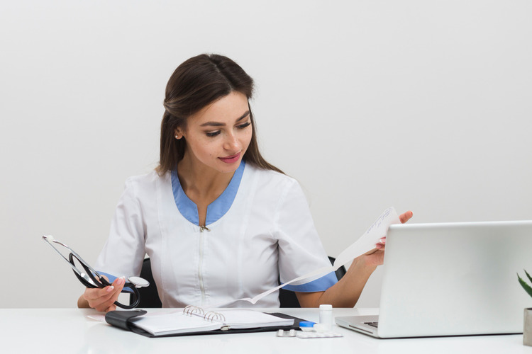 image of a female medical underwriter working on a laptoip with a paper in her hand; concept of jobs after bpharm