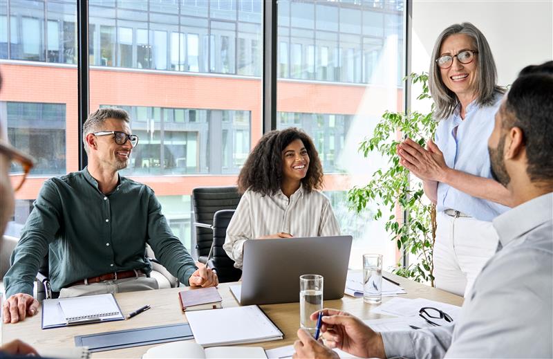 Senior older female executive ceo and happy multicultural business people discuss corporate project at boardroom table. Smiling diverse corporate team working together in modern meeting room office.