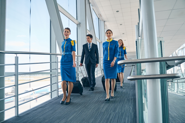 Cheerful stewardesses and their male colleague walking along the airport terminal