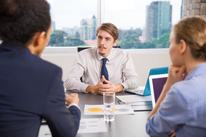 a high quality photograph of a caucasian male interviwer sitting with a laptop talking to candidates